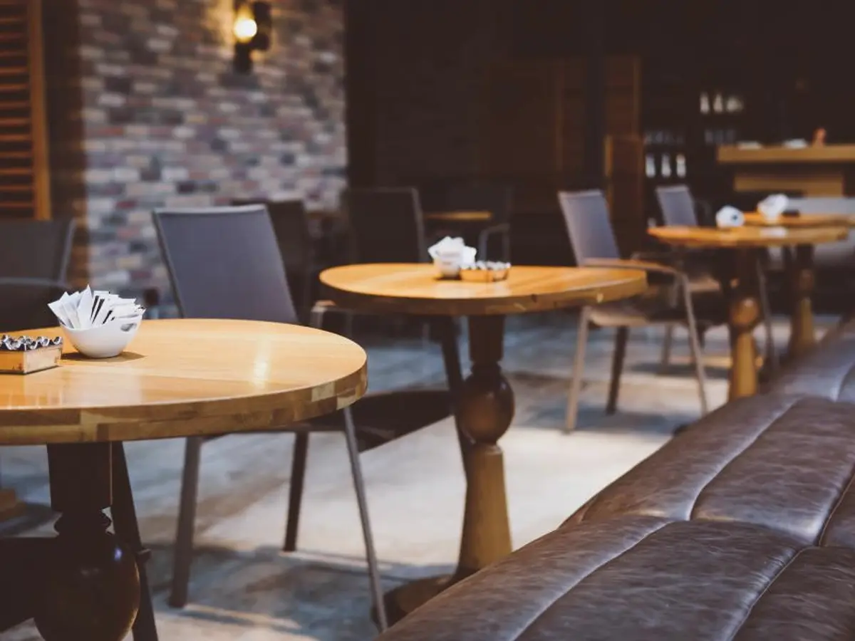 Restaurant dining room with round wooden tables laid out and a leather bench, with nobody free to answer the phone.